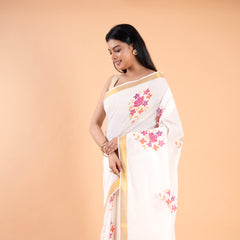 Woman wearing a white saree with floral patterns on a beige background