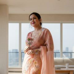 Woman in a pink saree with floral patterns against a green and beige wall.