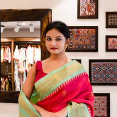 Woman in a pink saree standing in a store with framed artworks on the wall.