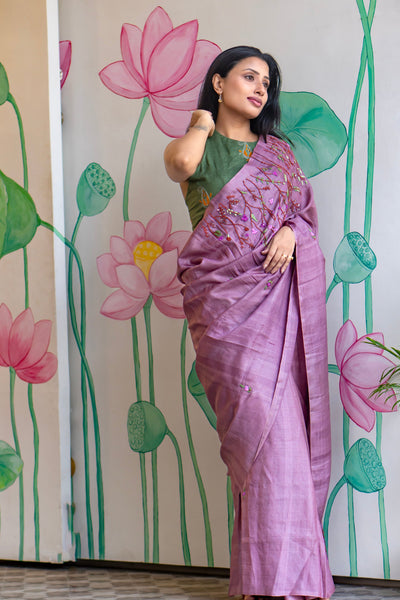Woman in a purple saree standing in front of a wall with lotus flower designs.