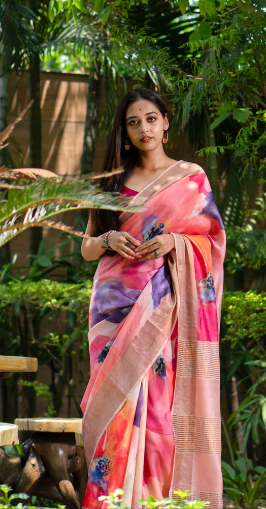 Woman in a colorful saree standing among lush greenery with yellow flowers.