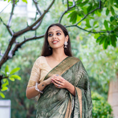 Woman in a green saree standing in a garden with trees and flowers.