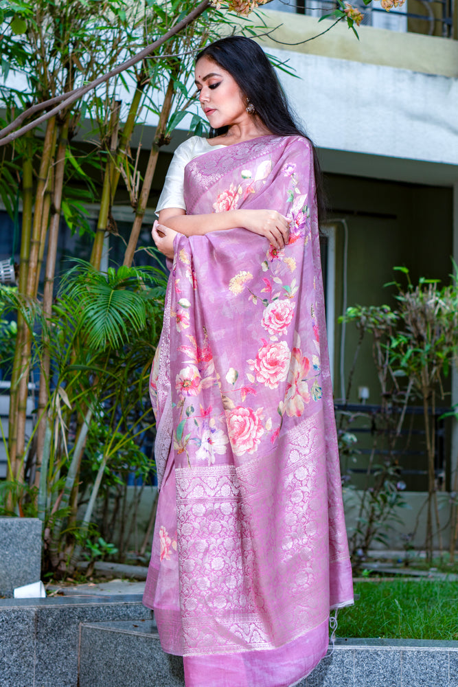 Woman wearing a pink saree with floral patterns outdoors.