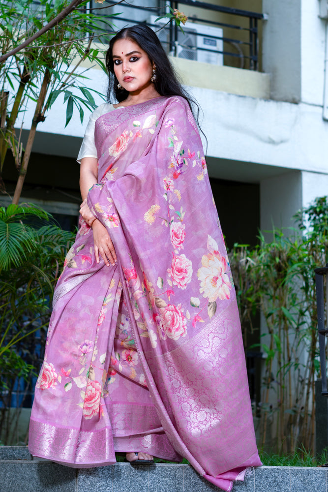 Woman wearing a pink saree with floral patterns standing outdoors.