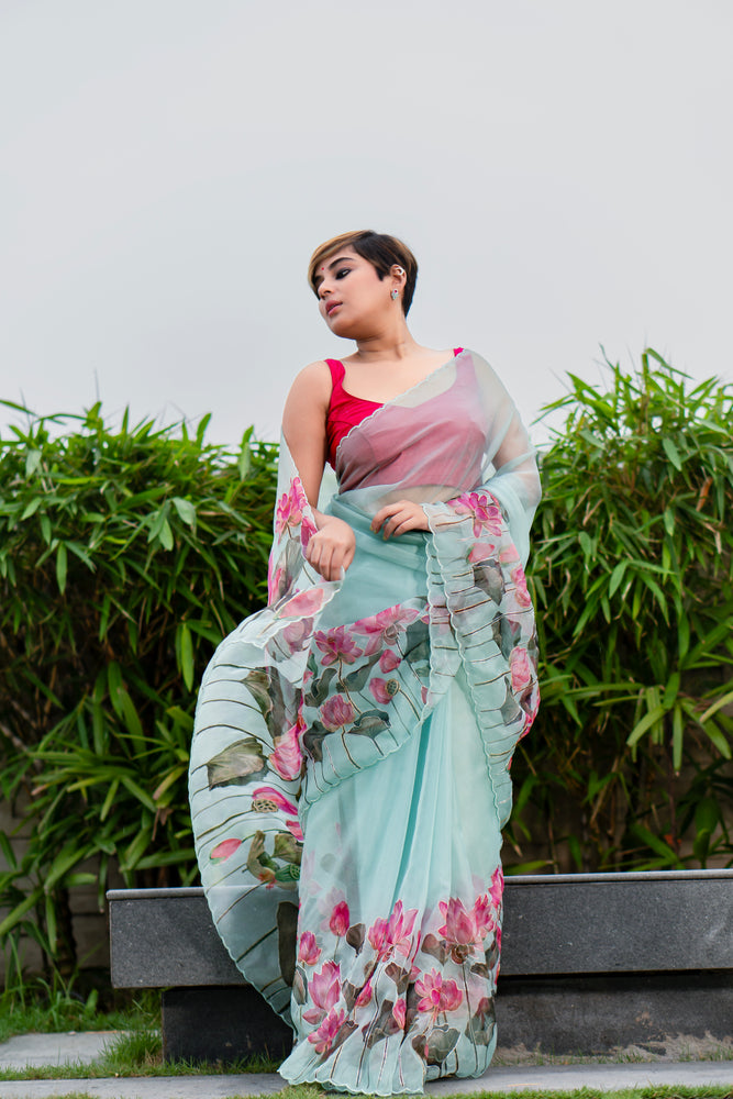 Woman wearing a floral saree with a pink blouse against a green foliage background