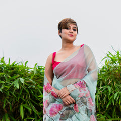 Woman wearing a floral saree standing outdoors with greenery in the background
